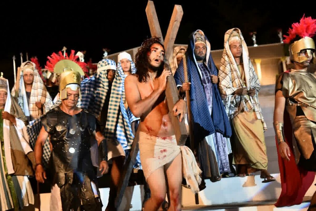 encenação de Jesus Cristo carregando cruz com várias pessoas ao redor